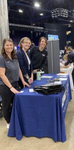 Three women standing at an informational table promoting the IL AHEC Network