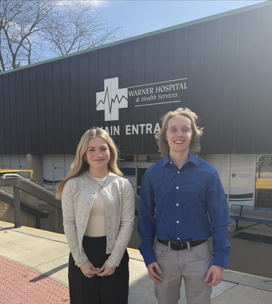 Two students standing in front of the Warner Hospital & Health Services sign