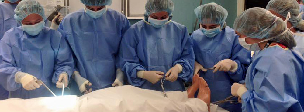 Wearing surgical gowns, caps, masks, and gloves, AHEC students practice operating room procedures.