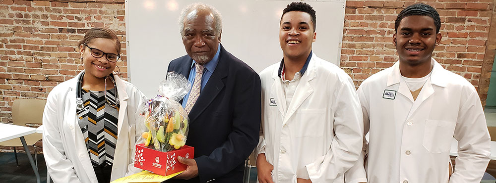 Illinois Congressman Danny Davis, holding flowers, poses with three Young Doctors Club members.