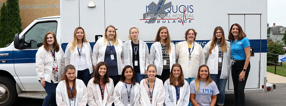 Young white-coated women pose in front of an Iroquois Memorial Hospital ambulance for a group photo.
