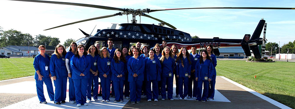 Students in blue jumpsuits pose on the landing strip with an Air-Evac helicopter.