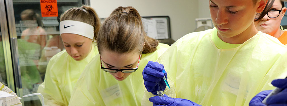 Students in yellow disposable polypropylene laboratory coats and blue nitrile gloves practice hands-on techniques in a lab.