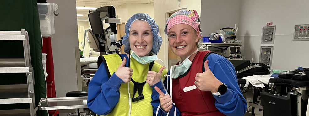 6-week preceptorship participants in gowns, safety aprons and PPE give the thumbs up in a gear-intensive part of the hospital.
