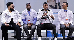 White-coated speakers on stage for a Black Men in White Coats presentation.
