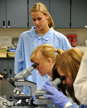 Participants in gowns and gloves look through microscopes.