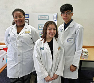 Young Doctors Club members pose in their white coats in front of facts they have assembled on diabetes.