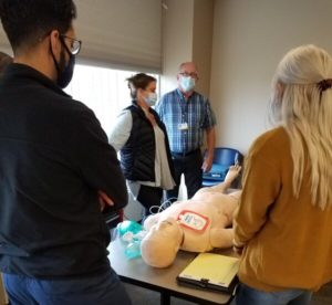 The advanced cardiac life support class, wearing masks, surround the new simulation manikin.