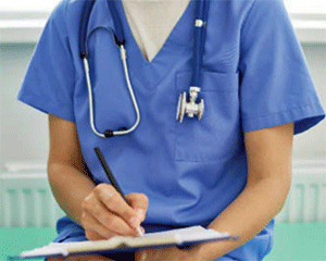 Figure in scrubs with stethoscope, seen from the neck down, making notes in a chart.