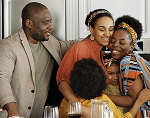 Parents and three kids, all in special-occasion clothes, have a group hug. Some wine glasses are visible.