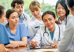 Young health professionals in scrubs gather around a facilitator with a stethoscope and a tablet device.
