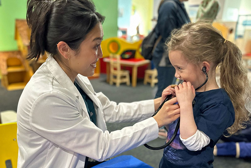 Medical student letting little girl discover what a stethoscope sounds like.