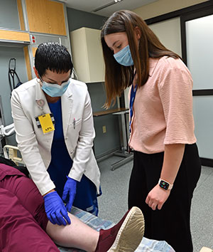 An advanced practice nurse shows a student participant how they examine a patient's leg.