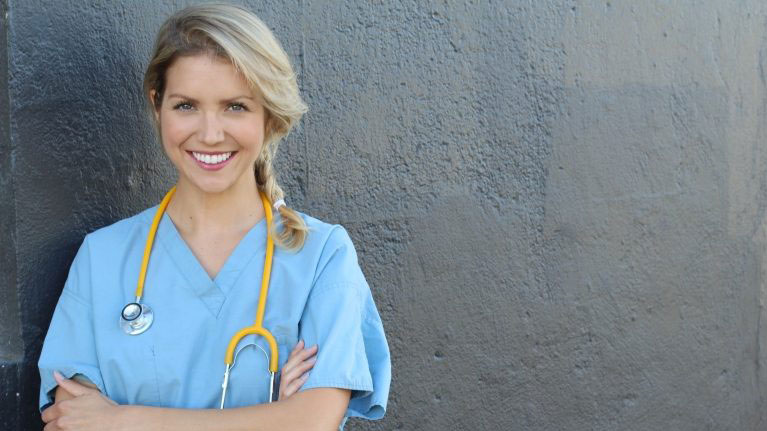 Smiling young health professional in pale blue scrubs with a stethoscope.