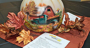 Fall centerpiece: pumpkin with painting of a blue pickup truck full of pumpkins in front of a red barn, surrounded by spray-painted autumn leaves. In the foreground, agenda for the 2017 Rural Health Day celebration.